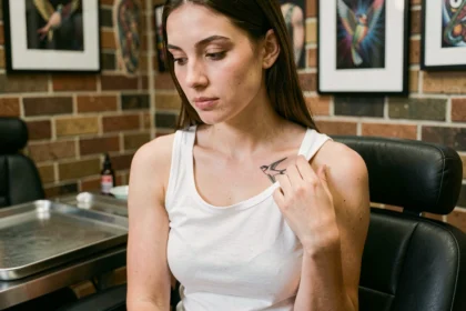 Jeune femme en studio de tatouage examinant un tatouage hirondelle sur l'épaule pour choisir la taille idéale