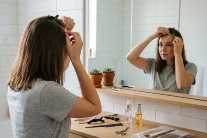 Femme posant des extensions adhésives sur ses cheveux devant un miroir de salle de bain